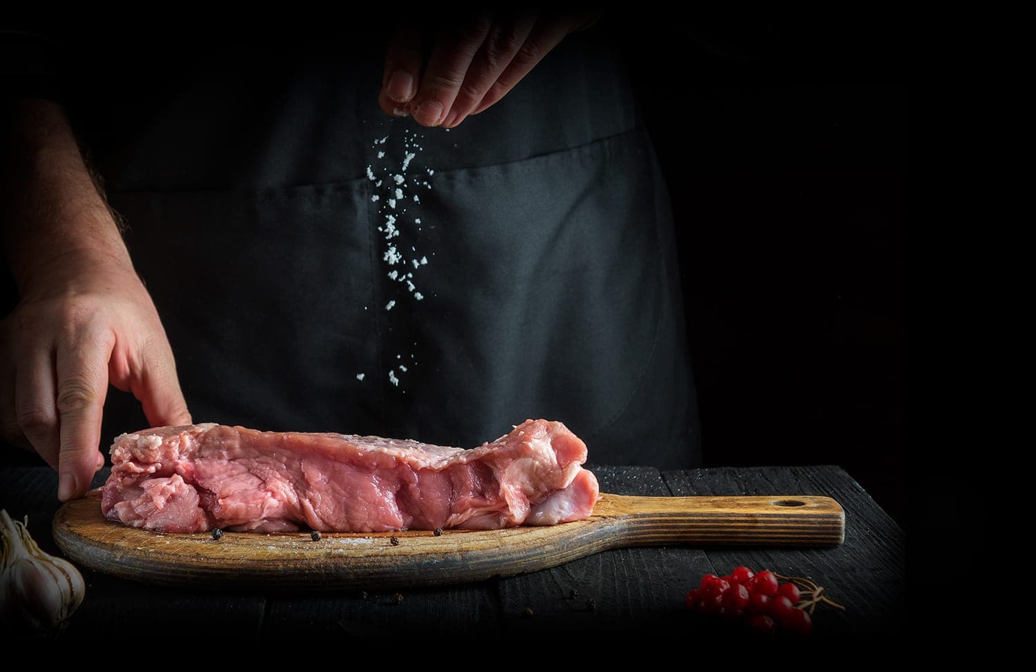 Chef assaisonnant un steak sur une planche en bois